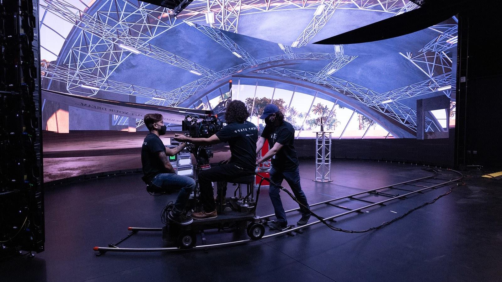 Crew members work on a dolly-mounted camera. 虚拟生产LED屏幕显示了飞机机库的内部