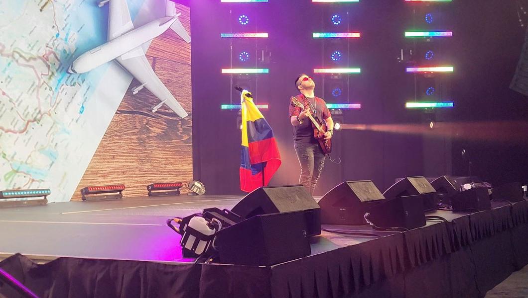 一个人在舞台上弹吉他，旁边的旗杆上插着哥伦比亚国旗.